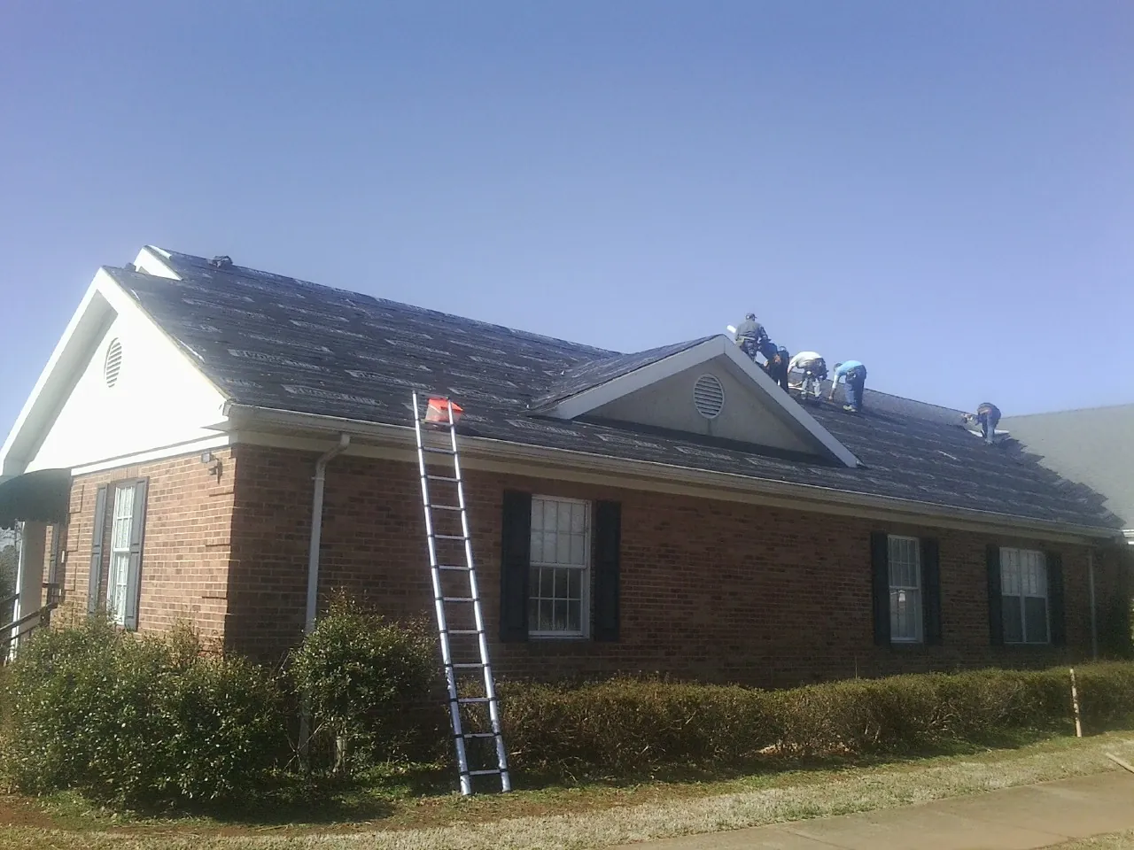 Crew tearing shingles off a brick ranch roof with a ladder set — Emergency Roof Repair work by our crew in Galway