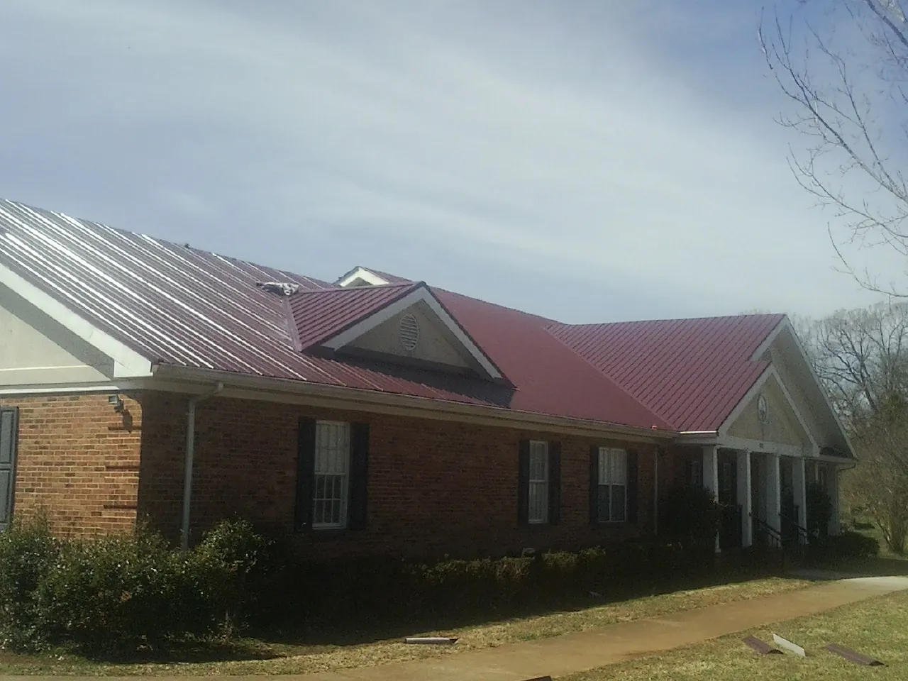 Red metal roof with gabled entries on a long brick building, from a Hail Damage Roof Repair job in Galway