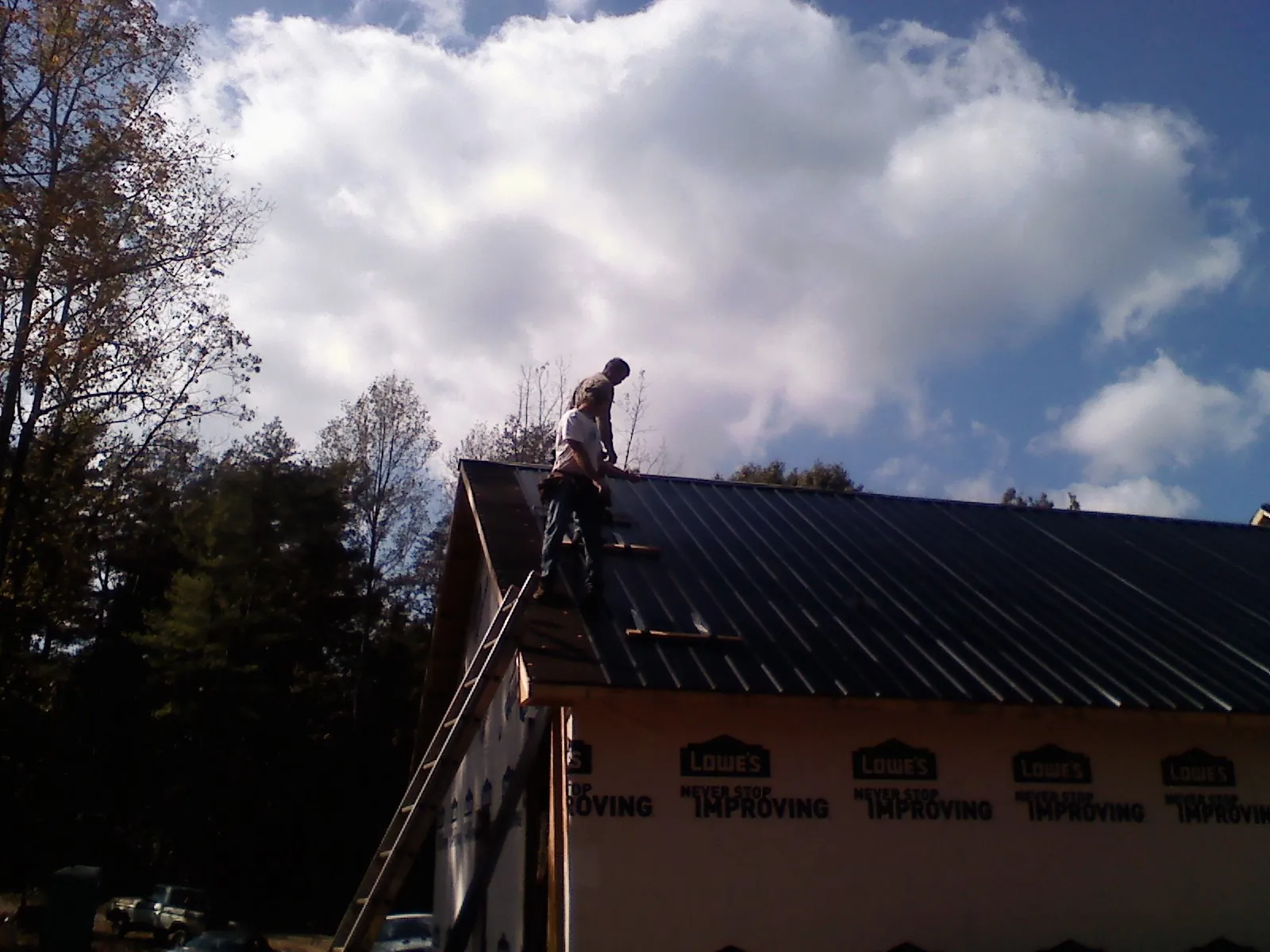 Roofer fastening dark metal panels high against a cloudy sky, from a Roof Inspection job in Galway