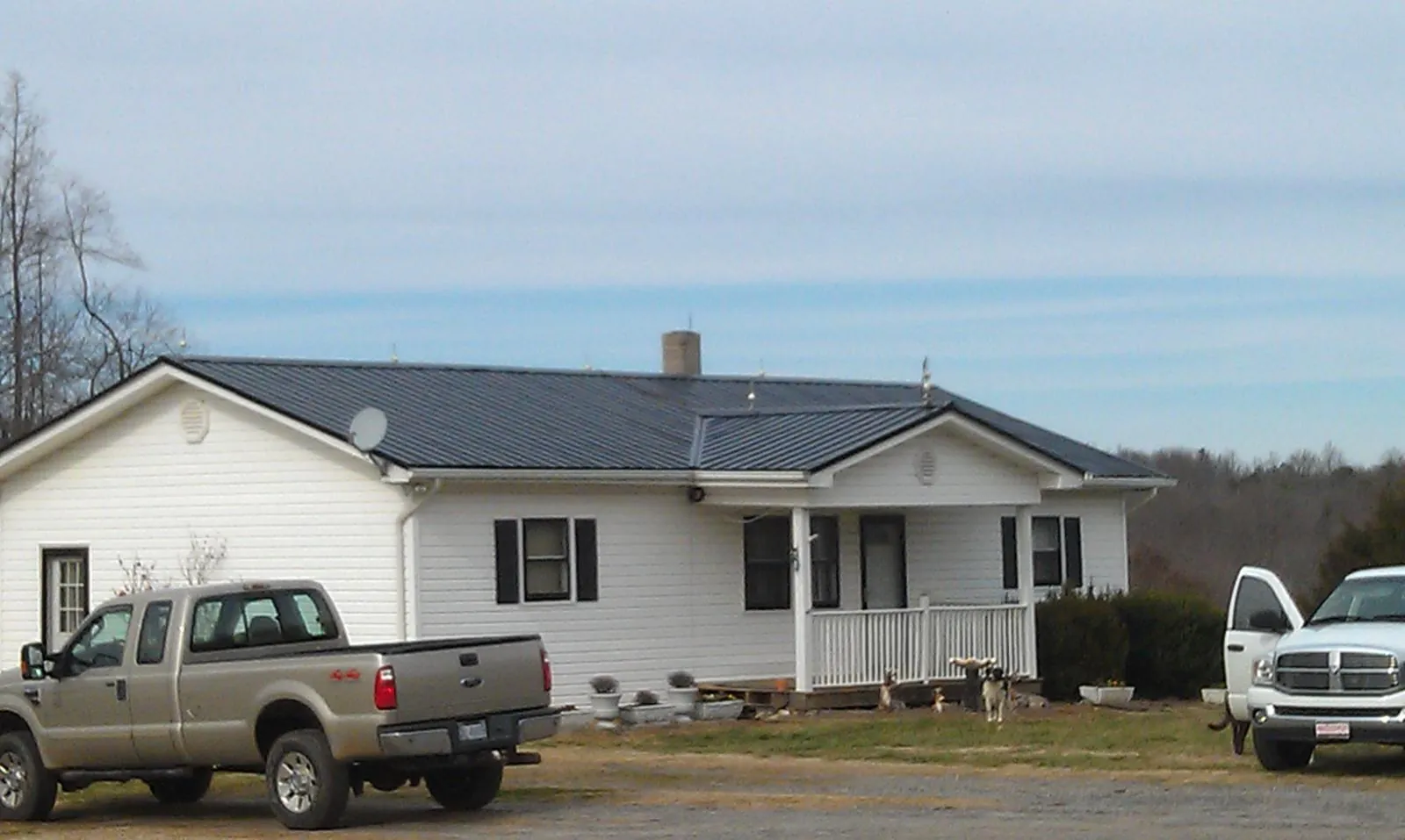 Finished dark metal roof on a white ranch home with work trucks parked in Galway