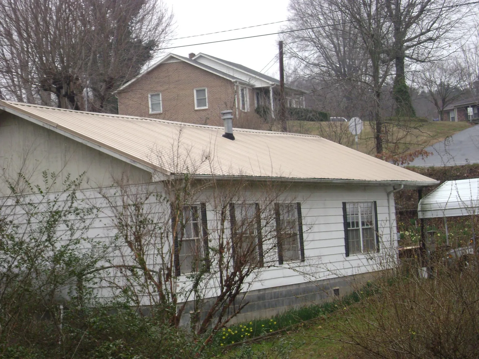 Tan metal roof on a white sided house set into a hillside — Commercial Roofing by Roofing Brothers in Galway