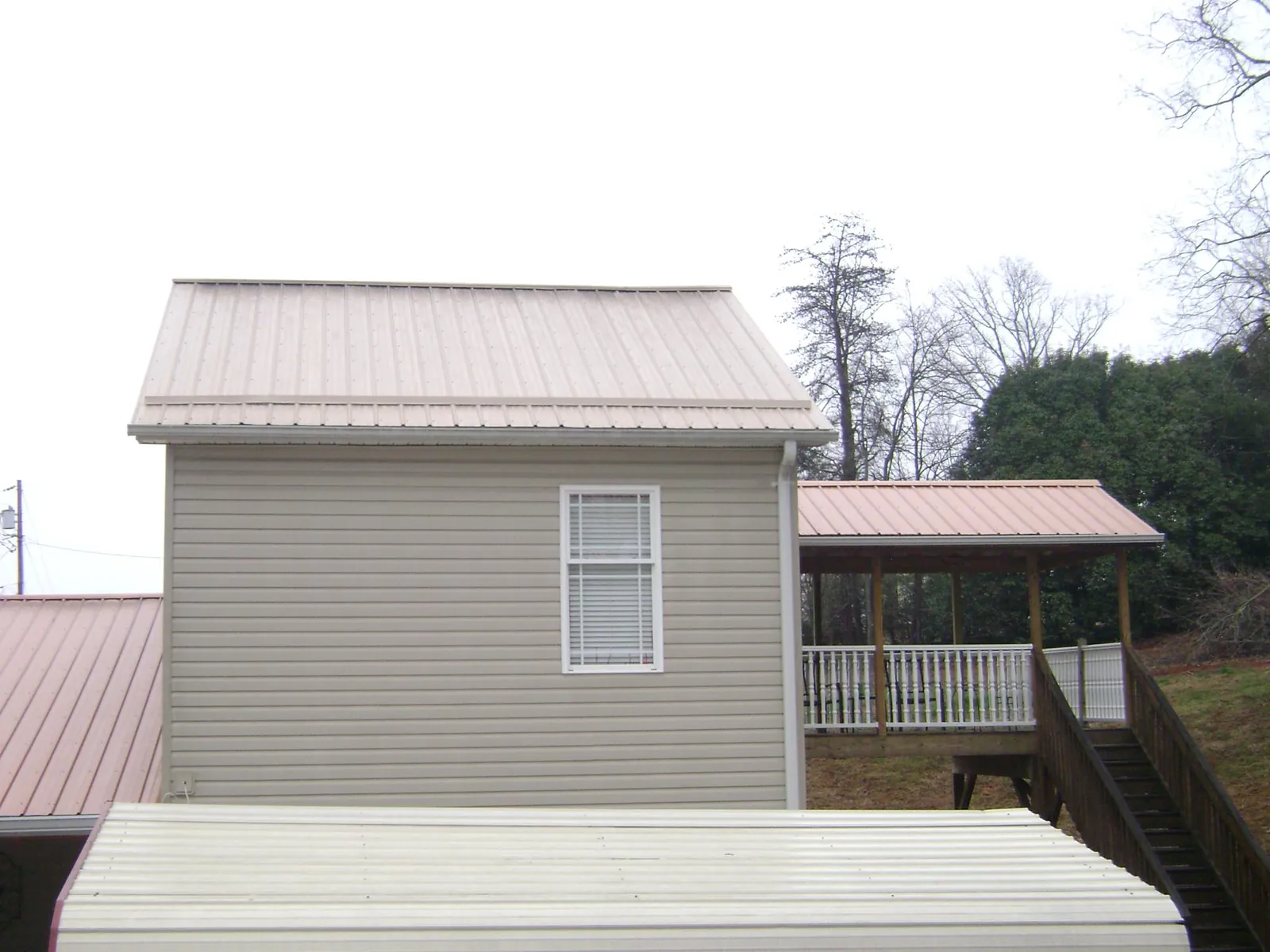 Tan metal roofs on a two story addition and attached porch, from a Roof Replacement job in Galway